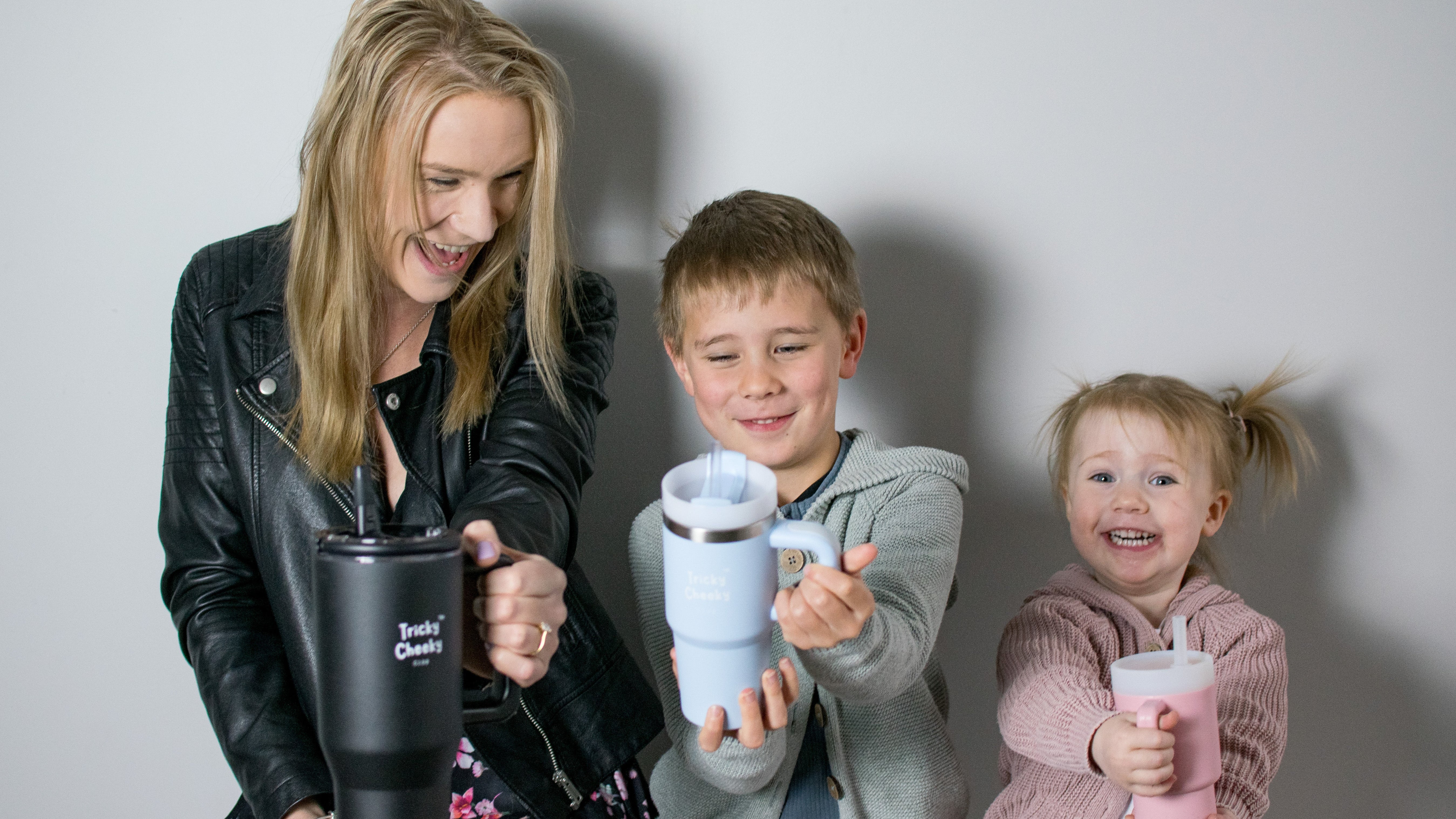 Woman and two children holding insulated cups against a plain background